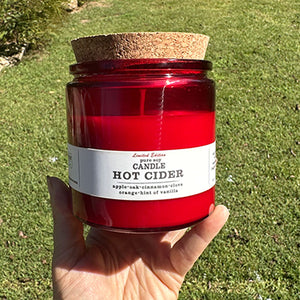 HOT CIDER SOY CANDLE - The warm scent of oak barrel apple cider combined with mulled spices of clove, cinnamon, hints of orange and vanilla. 100% soy candle. Handmade by Turnrow Bath, Body &amp; Home in Georgia. Comes in red glass vessel with cork lid that can be reused as a planter or holder for treasures. 10 oz. 30 hr + burn time. Photo creidt: Turnrow Bath, Body & Home